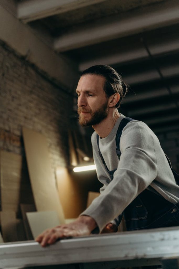 Bearded carpenter meticulously working indoors in a woodworking shop.